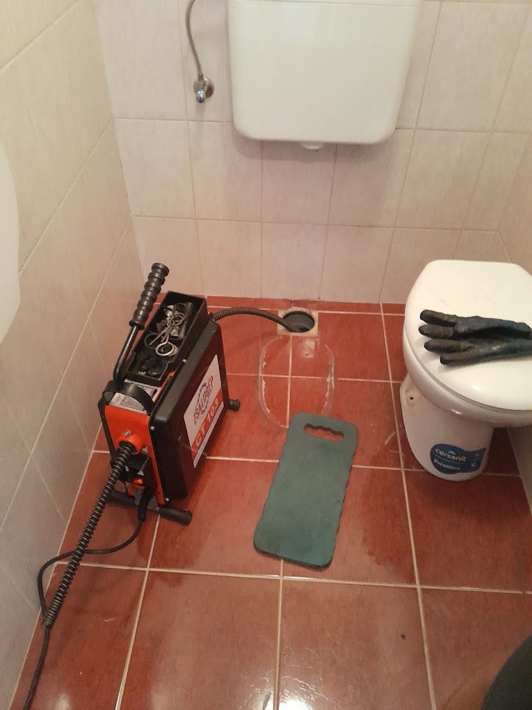 Gép a WC mellett a padlón, mellette térdvédő